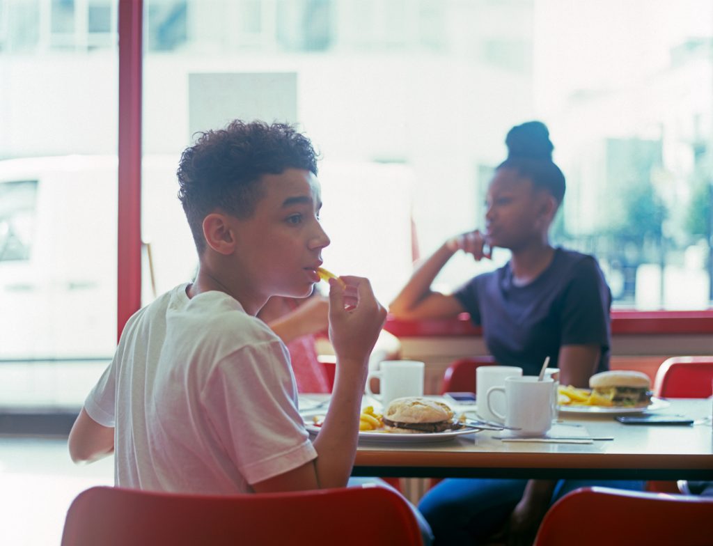Teenage boy in a restaurant eating a hamburger and french fries