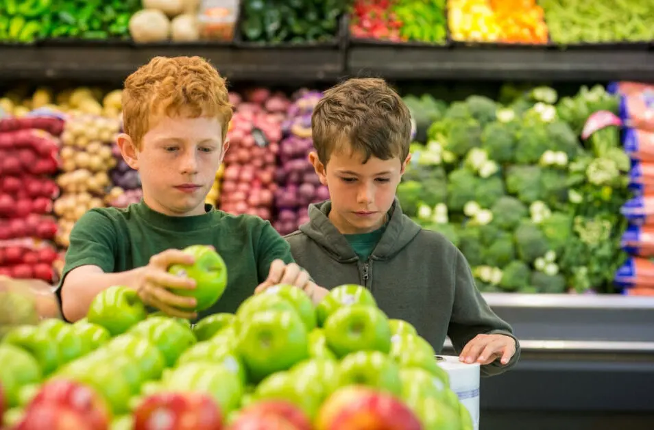 Two children picking out an apple at the grocery store.