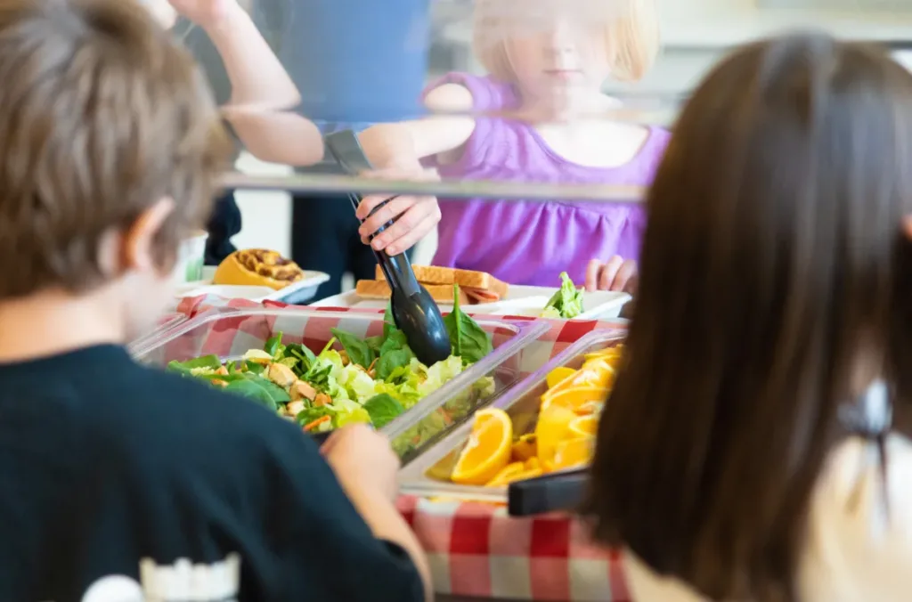 Kids use tongs to grab salad for a school lunch