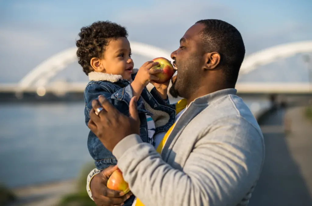 A dad carries his son, who feeds him an apple