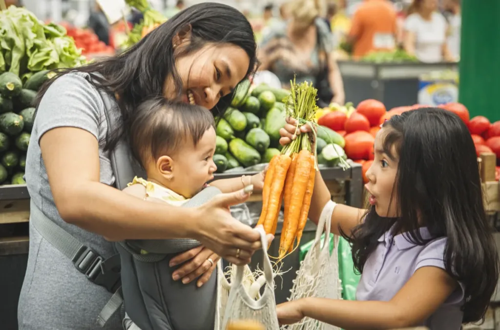 A mom and her two children buy fresh vegetables